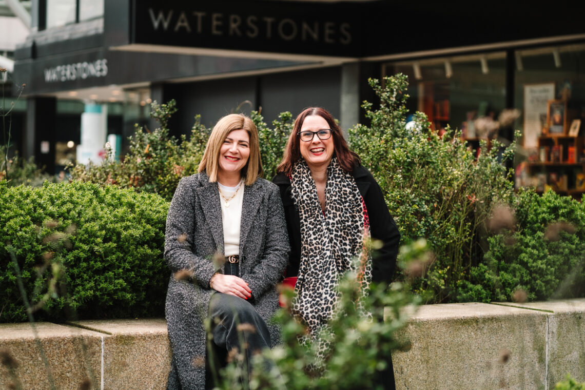 Kate and Emma from Piece of Cake Marketing sat on a wall next to each other in Coventry City Centre.